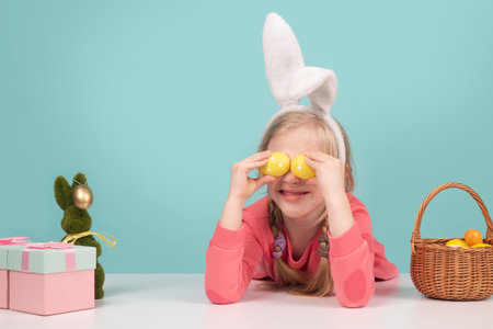 Cute little child wearing bunny ears on Easter day. Girl holding painted eggs on eyes. Easter kids holiday.の写真素材