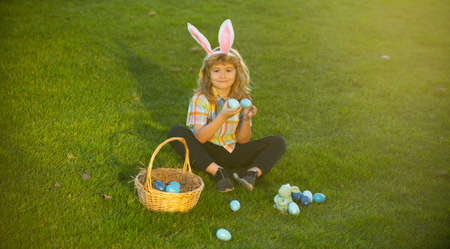 Child with easter eggs in basket outdoor. Boy laying on grass in park. Easter egg hunt. Fynny kids...