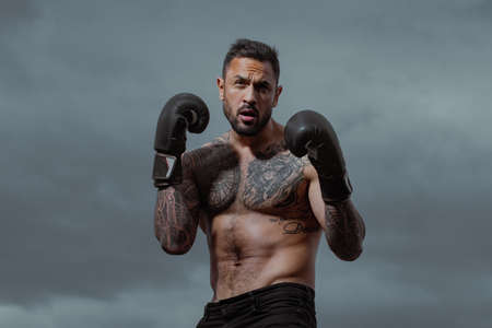 Muscular kick boxer or muay thai fighter punching. Kickboxing fighter in boxing gloves hitting...