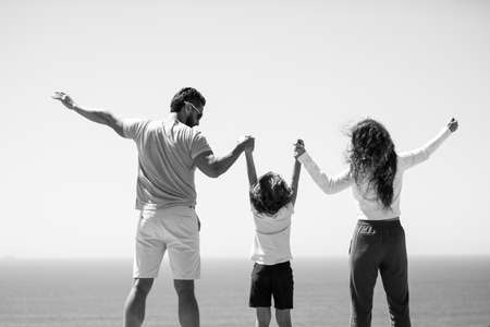 Back view of happy young family walking on beach. Child with parents holding hands. Full length poeple.の写真素材