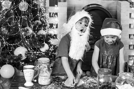 Christmas family. Happy new year. Funny children chefs in santa hats prepare holiday food. Funny kids are preparing the dough playing with flour in the kitchen.の写真素材