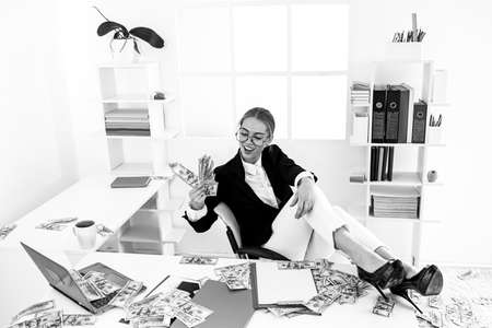 Funny businesswoman with money dollar banknotes working on the desk at office.