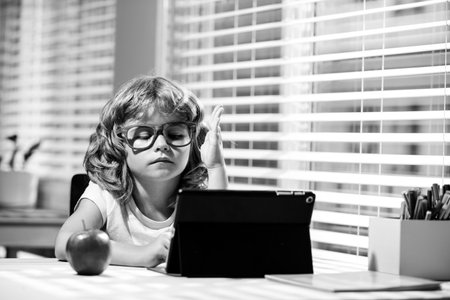 Kid at home schooling. Online school. A smart boy sitting at the table, writing homework or...
