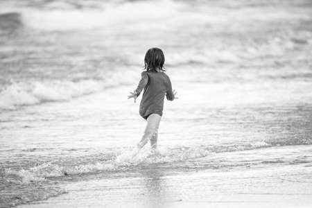 Blonde boy running and having fun on the beach on blue sea in summer.の写真素材