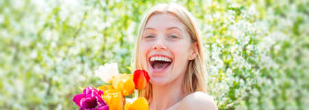 Spring woman face for banner. Happy woman relaxing in the tulip fields. Womens day, 8 march. Field of colorful bright red tulips. Laughing girl.の写真素材