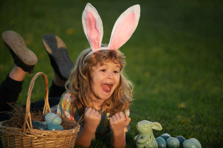 Child bunny boy with rabbit bunny ears. Child with easter eggs in basket outdoor. Boy laying on...