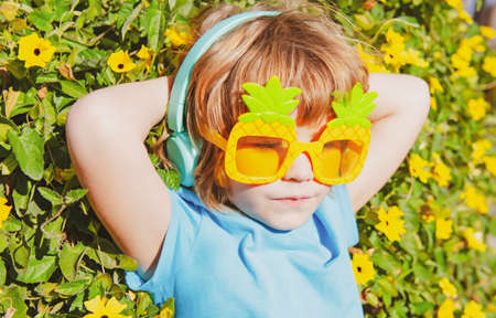 Funny summer mood. Happy kid in crazy glasses and headphones. Happy boy in party sunglasses.