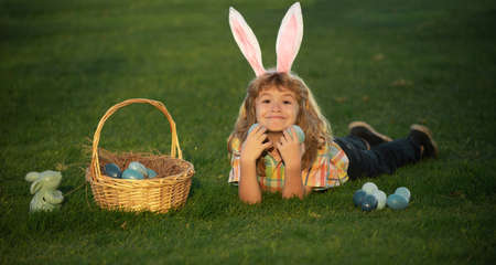Child boy hunting easter eggs in spring lawn laying on grass. Bunny kids with rabbit bunny ears.