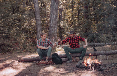 Vacation weekend picnic camping and hiking. Two young guy sitting in the forest and drinking beer...