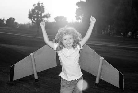 Amazed excited kid playing with toy plane on sunny golden sunset sky background outside on grassy summer hill. Dreaming about happy future concept. Expression kids face.の写真素材