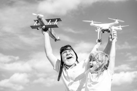 Excited grandson child and funny amazed grandfather with plane and quadcopter drone over blue sky and clouds background. Men generation granddad and grandchild.の写真素材