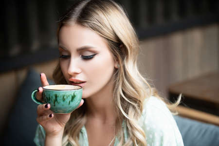 Close up portrait of blonde young woman with cup coffee. Girl holding near her lips a cup of hot...