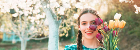 Spring woman face for banner. Beautiful girl gardener with flowers. Funny girl planting vegetable in home garden field, relax outdoor activities. Spring blossom background.の写真素材