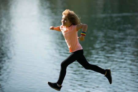 Child boy running or jogging near lake on grass in park. Outdoor sports and fitness for children, exercise outside. Sporty child jogging in a park. Outdoor sports and fitness for children.の写真素材