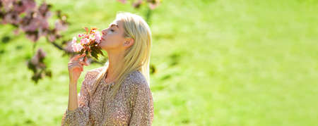 Spring girl fashion. Woman with pink cherry blossom in summer day. Beauty young woman enjoying nature in spring sakura garden. Spring design for banner or website header, copy space.の写真素材