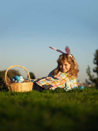 Child boy hunting easter eggs in spring lawn laying on grass. Cute bunny child boy with rabbit ears...