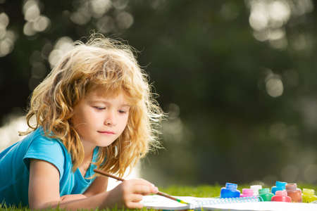 Children artist paints creativity vacation, kids crafts. Child boy drawing in summer park, painting art. Little artist painter draw pictures outdoor.の写真素材