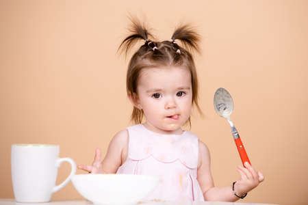 Kid eat healthy nutrition, baby food. Babies eating with spoon. Funny baby girl with spoon on studio, isolated.の写真素材