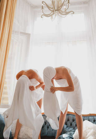 Funny young woman in pajama morning leisure time in bedroom at home. Excited girlfriends in white bathrobes and towels in bedroom.の写真素材