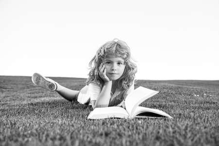 Funny kid reading the book in spring park. Child boy is reading a book on the spring park. Relaxing on the grass in the garden. Outdoor education.の写真素材