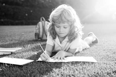 Cute childr boy with books with pencil writing on notebook outdoors. Summer camp. Kids learning and...
