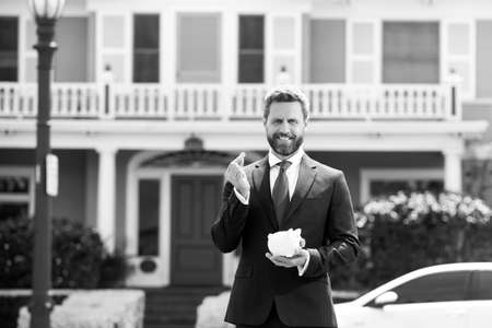 Man holding piggy bank on rich house background. Save money and financial investment.の写真素材