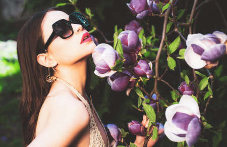 Vogue fashion style portrait of young girl. Fashion female model with sunglasses outdoor. Magnolia flower background.の写真素材