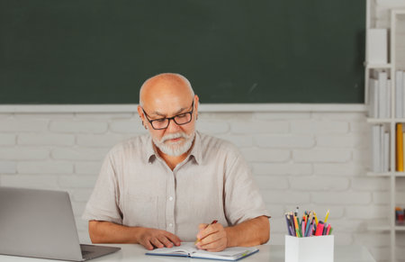 Aged male retired teacher. Portrait of mature teacher or tutor professor working at table in college or high school.の写真素材