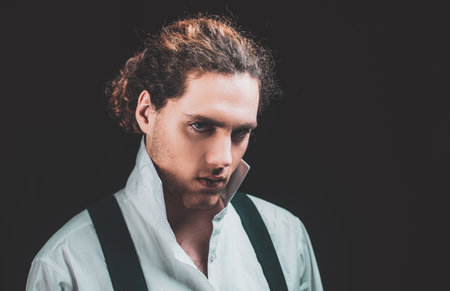 Handsome curly brunet. Young man tense face in white shirt. Barbershop advertising. Man with confident face and brutal style isolated on black background.の写真素材