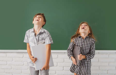 School children hold book with surprising expression against blackboard. School kids friends.の写真素材