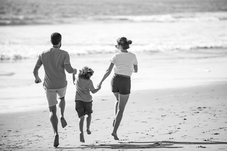 Back view of family run on the beach. People having fun on summer vacation. Father, mother and child...