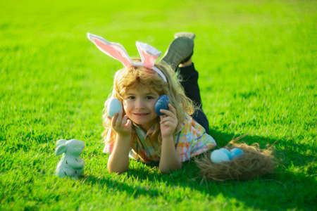 Easter bunny children with rabbit ears in garden hunt egg. Child hunting eggs wear bunny ears hold Easter eggs laying on grass in park.の写真素材