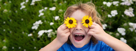 Banner with spring child face. Funny Boy Kid and Daisies. Happy little blond hair child with flowers eyes on the grass with daisies flowers. Child dreaming and smiling against camomile field.の写真素材