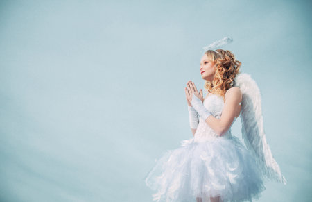 Cherub. Valentines day pray cupid. Heaven. Happy teenage angel girl pray. Festive Art Greeting Card. Girl angel with halo in white angel dress. Cute teen cupid on the cloud - heaven background.の写真素材