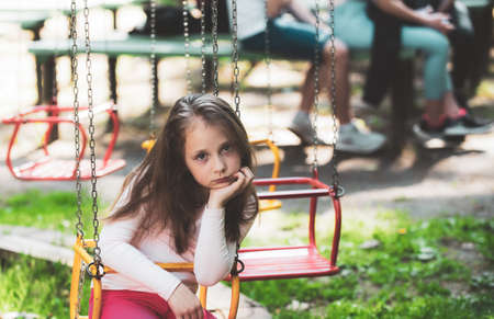 Little girl having fun on a swing outdoor. Sad girl sitting alone on a swing in a park playground....
