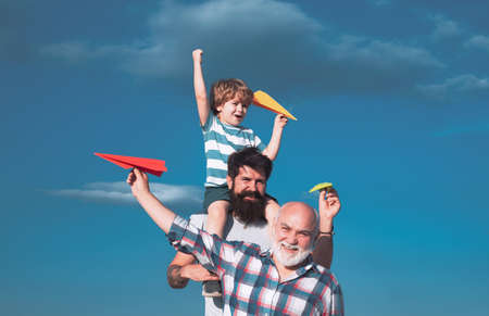 Happy three generations of men have fun and smiling on blue sky background. Father and son playing outdoors. Airplane ready to fly. Cute son with dad playing outdoor.の写真素材