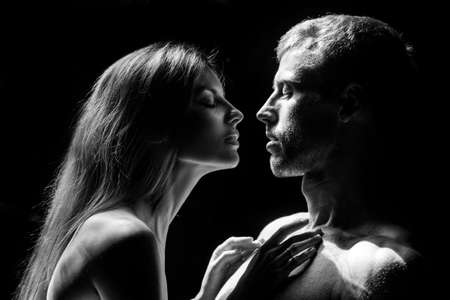 Man embracing and going to kiss sensual woman. Loving couple kissing over black background. Real...