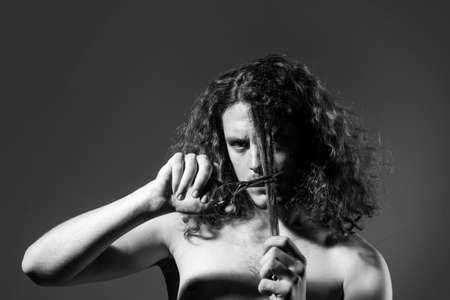 Young sexy man, portrait of guy with scissors cut long curly hair. Modern barbershop, shaving. Handsome male with modern hairstyle on black.の写真素材