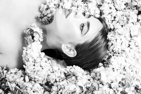 Beauty Woman lying on flowers. Blossom Makeup cosmetics and skincare. Girl with hydrangea flowers.