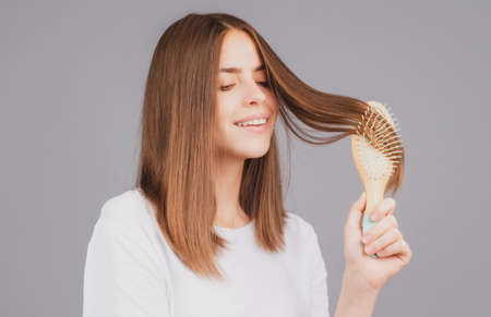 Brushing Hair. Portrait young smiling woman brushing straight natural hair with comb. Girl combing hair with hairbrush. Hair care beauty concept.の写真素材