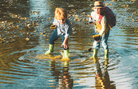 Little boy and girl throws stones into the water on the shore of a lake. Children throw stones at the water. Beautiful children throws a rock at the river. Skipping Rocks.の写真素材