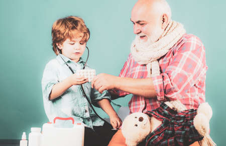 Family doctor. Man in knitted colorful scarf with medicine. Happy little boy in doctor costume holding stethoscope on color background.の写真素材