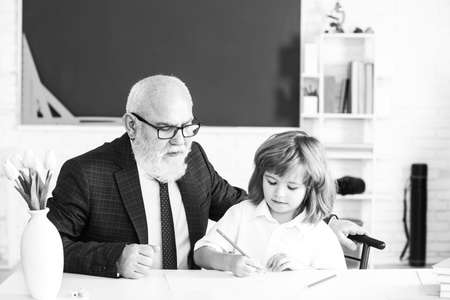 Old professor or senior teacher teaching little school boy. Educational conversation. Talking to students or pupils. School teacher concept.の写真素材