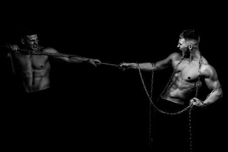Two Men broken chains, holding chain. Sexy torso of young fitness man with muscular strong abdominal and pectoral muscles and powerful breast. Isolated on black.の写真素材