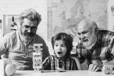 Three generations of men having fun together. Grandfather teaching grandson how to play Jenga games.の写真素材