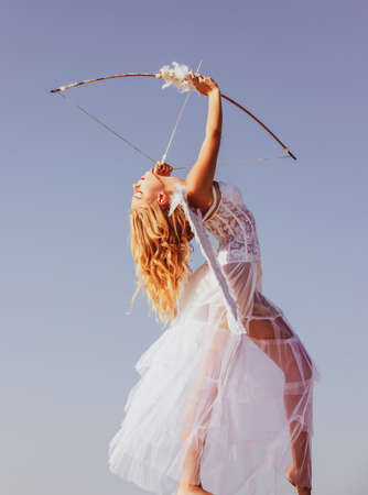 Valentines day. Angel cupid with bow and arrow. Woman in white dress. Portrait of sweet angelic girl.の写真素材