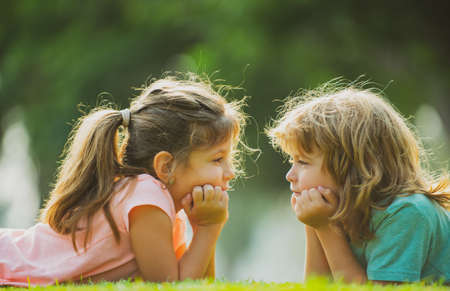 Brother and sister having fun in the park, two cheerful children laying down on green grass. Happy...