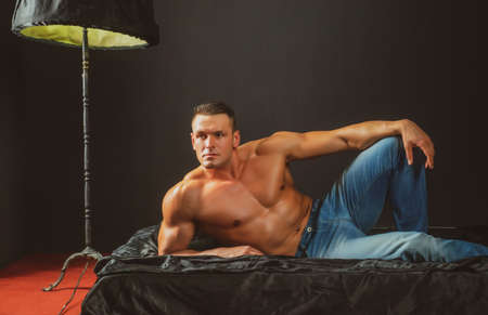 Portrait young sexy men bodybuilder athlete, with a bare torso, lies on a bed in pillows in...