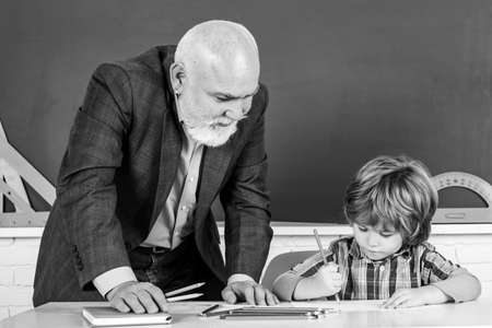 Senior teacher with pupil at back of classroom at the elementary school. Child at school lesson with senior teacher.の写真素材