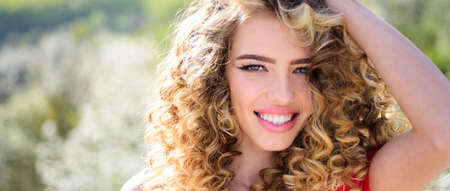 Spring girl with curly hair smiling. Beauty young woman enjoying nature in spring garden. Banner...